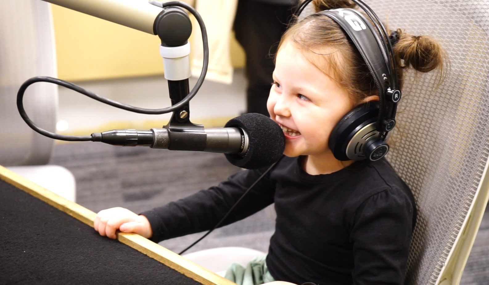 Young girls smiles as she talks in to the studio microphone, she is also wearing earphones